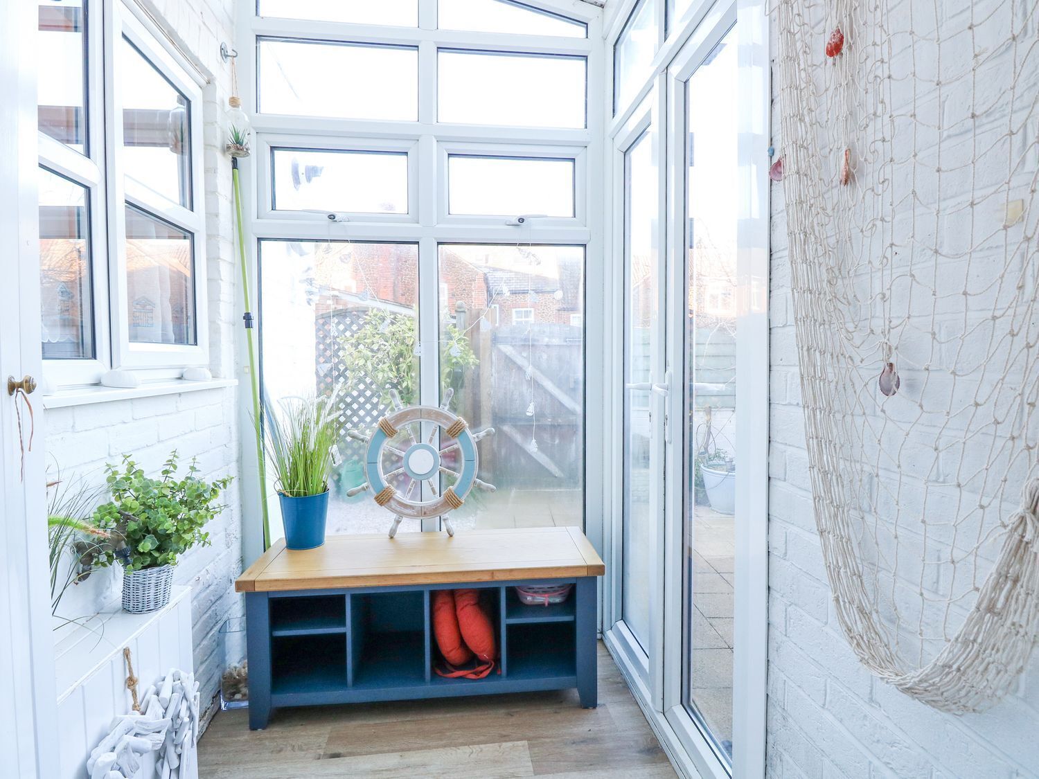 A sunlit room with a wooden bench, potted plants, and a ship's wheel decoration.