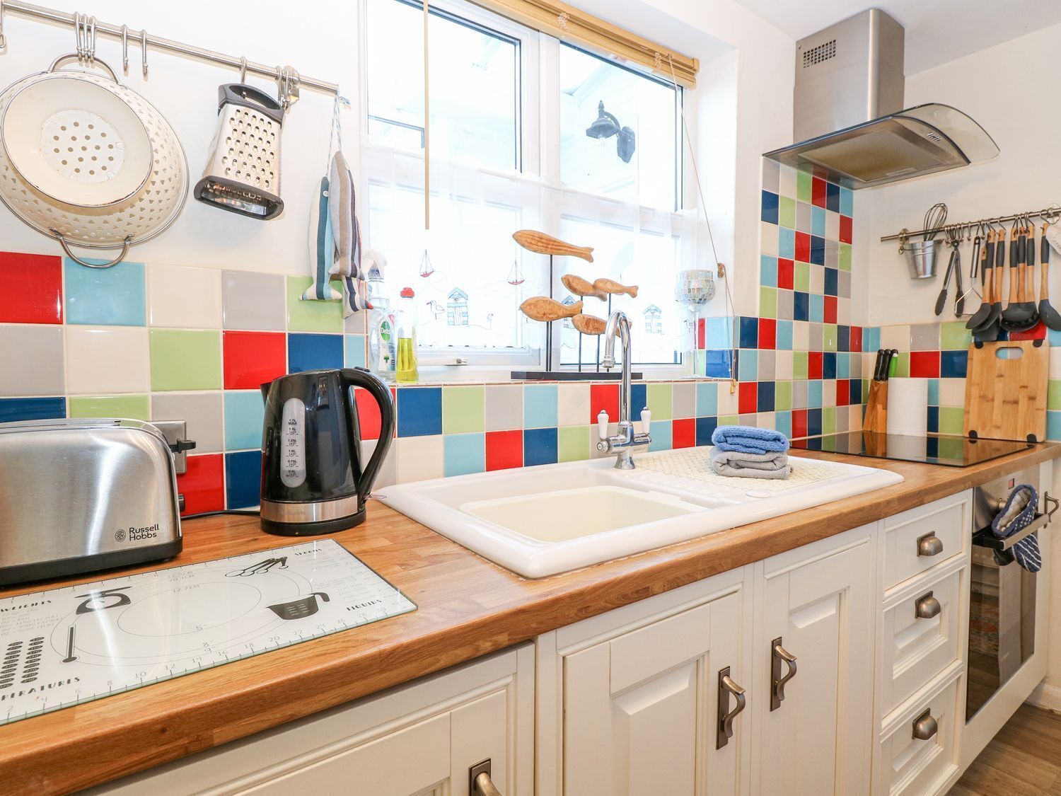 A kitchen with a wooden countertop, a kettle, a toaster, and a colorful backsplash.