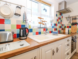 A kitchen with a wooden countertop, a kettle, a toaster, and a colorful backsplash. - Hideaway Cottage (Hunstanton)