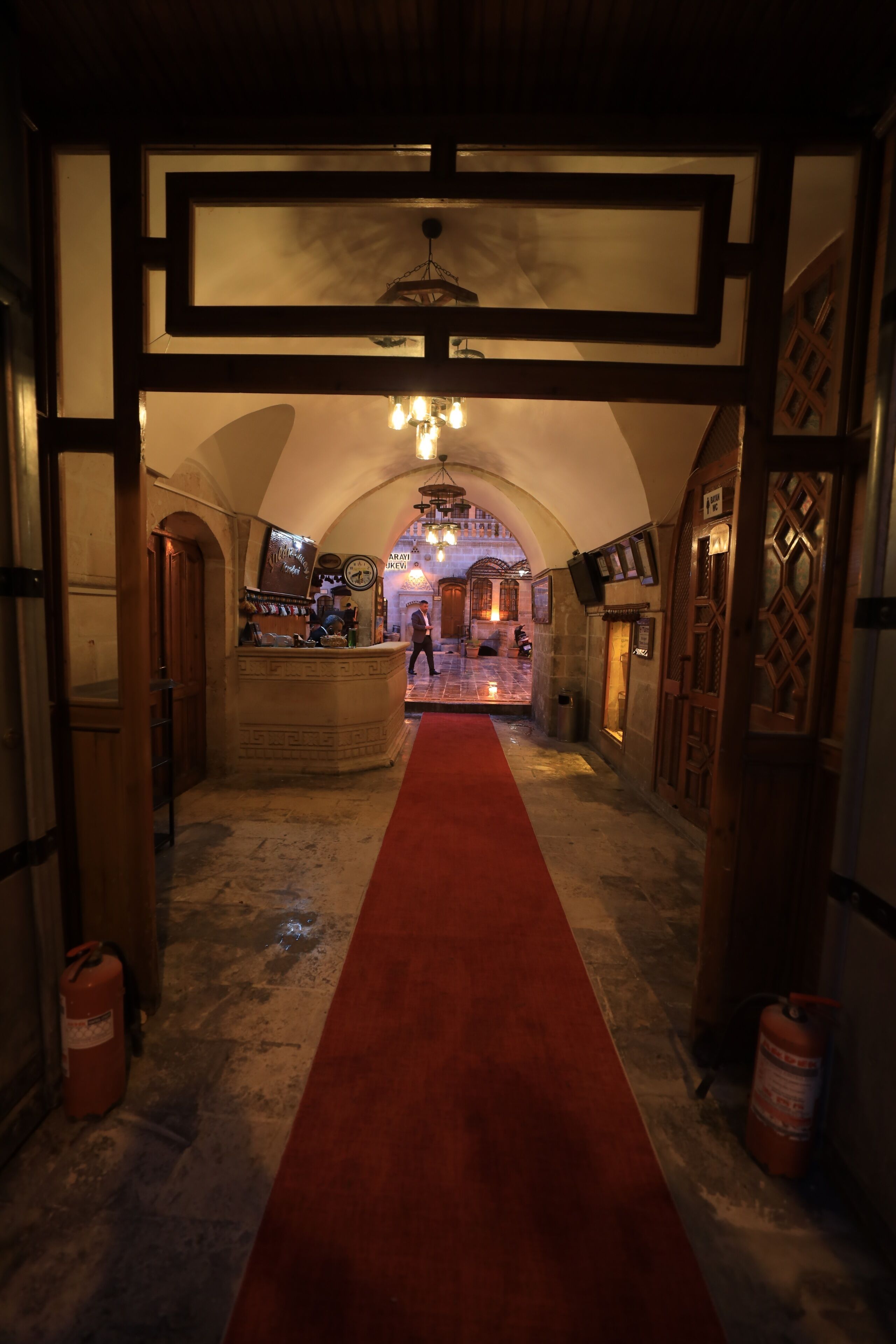 A corridor with a red carpet, wooden doors, and a reception desk in the background.