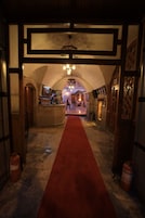 Un pasillo con alfombra roja, puertas de madera y un mostrador de recepción al fondo.