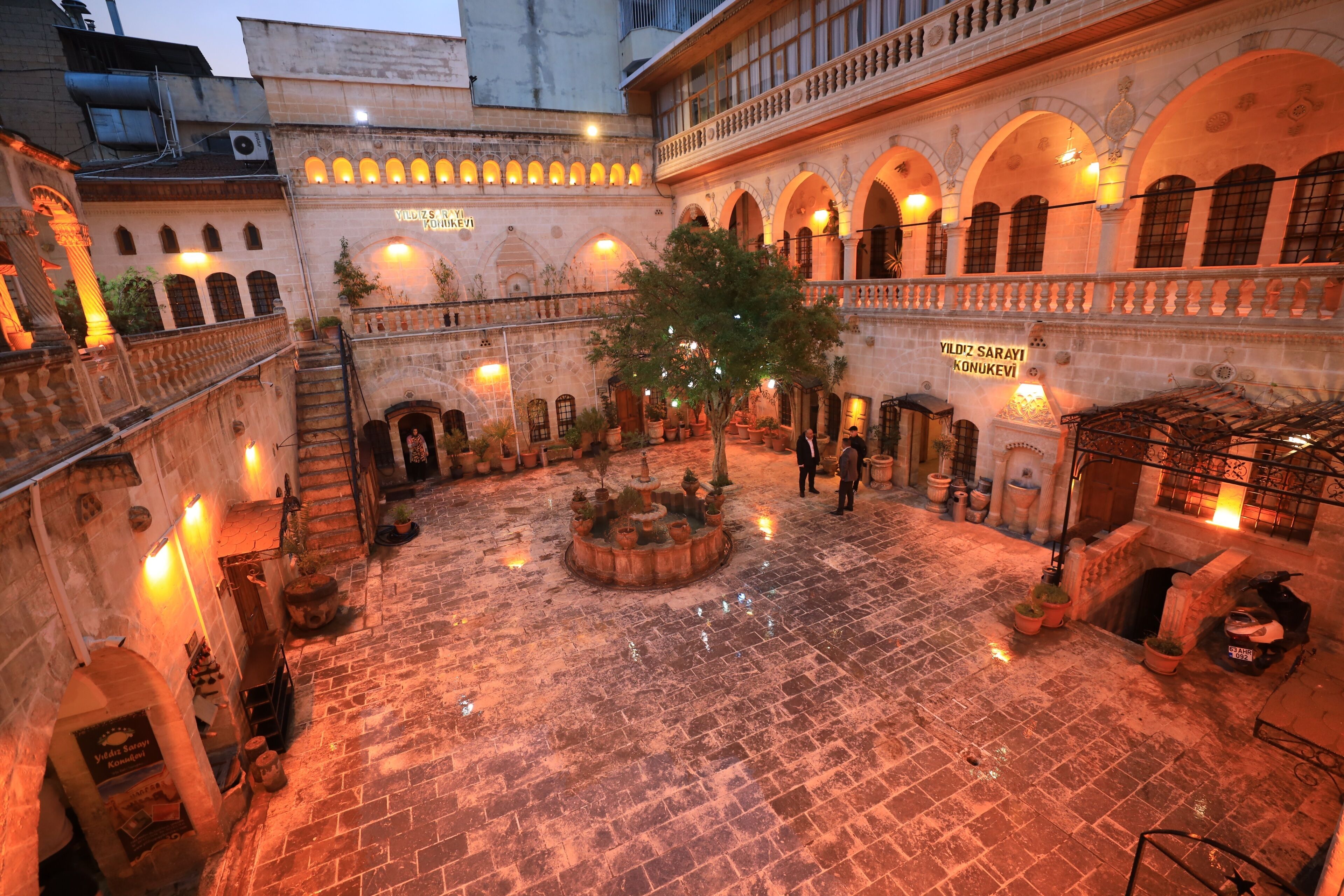 A courtyard with a fountain, potted plants, and a sign reading 'Yildiz Sarayi Konukeleri'.