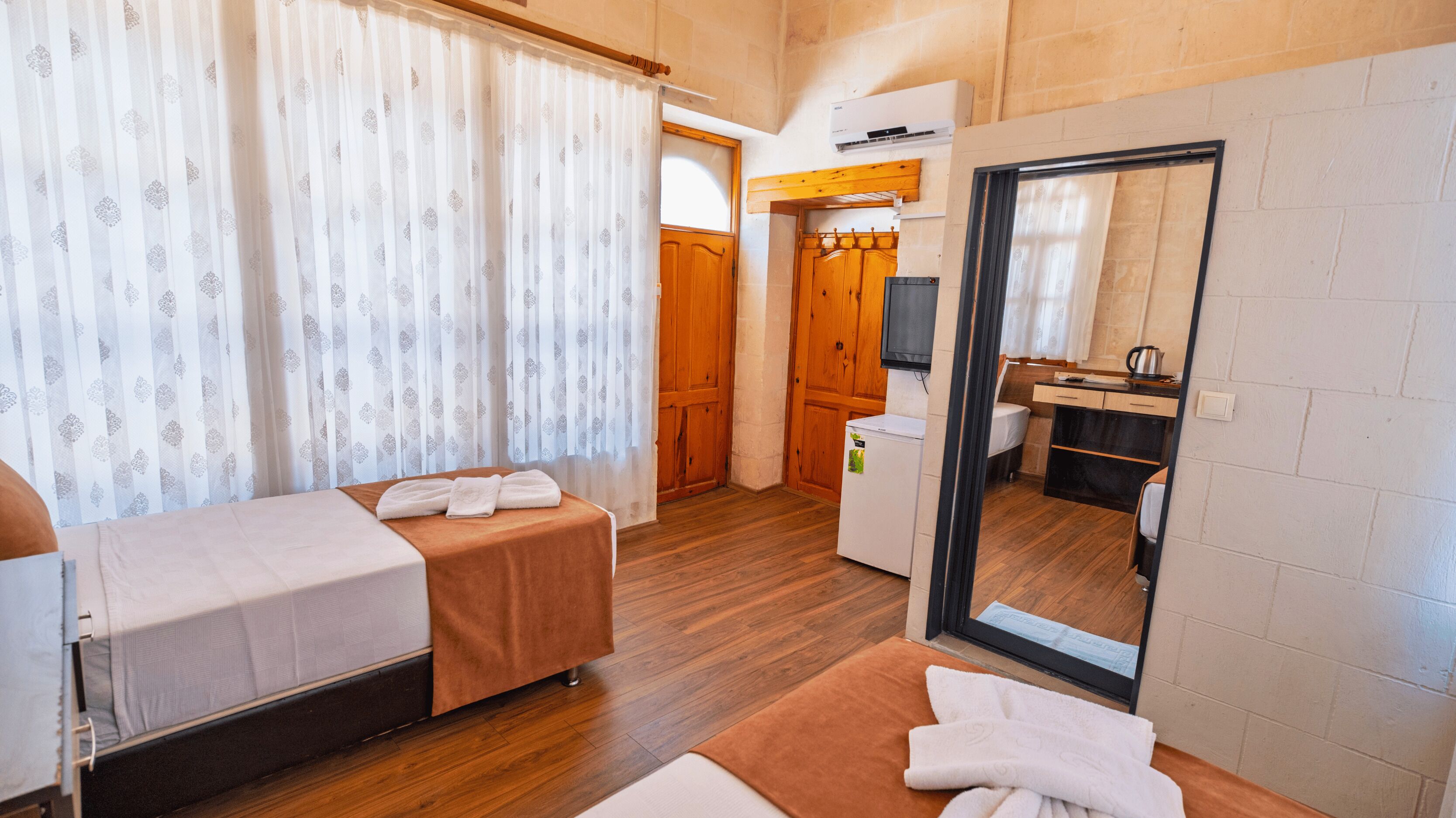 Una habitación compacta con cama, una mesita con toallas, un espejo y una pequeña zona de cocina.