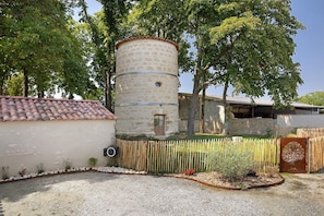 A stone tower with a circular base and a flat roof, surrounded by a wooden fence and trees. - House 'Le Moulin des Chouettes' with Jacuzzi in a Unique Setting (La Jarrie)