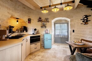 Una cocina rústica con vigas de madera, un refrigerador antiguo y un comedor con una mesa dispuesta para una comida.