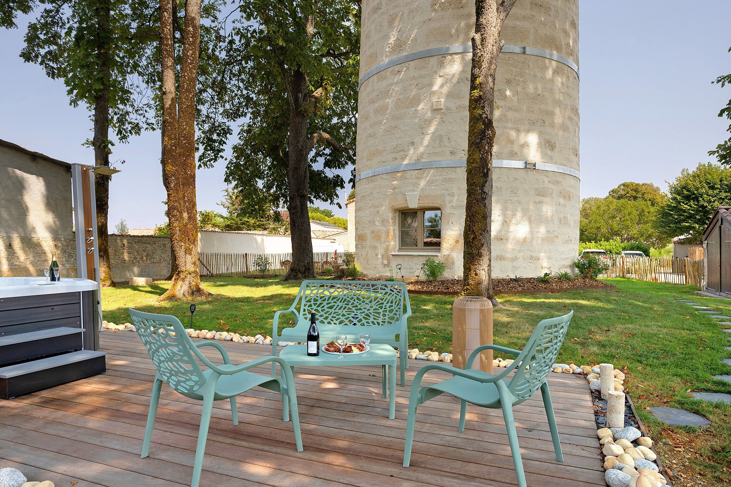 Une terrasse extérieure avec un jacuzzi, deux chaises et une table pour deux personnes, agrémentée de verres à vin et d’une bouteille.