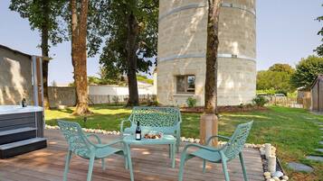 Une terrasse extérieure avec un jacuzzi, deux chaises et une table pour deux personnes, agrémentée de verres à vin et d’une bouteille.