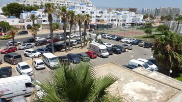 Un estacionamiento con varios coches y algunas camionetas, rodeado de palmeras y edificios de fachadas blancas y cúpulas azules.