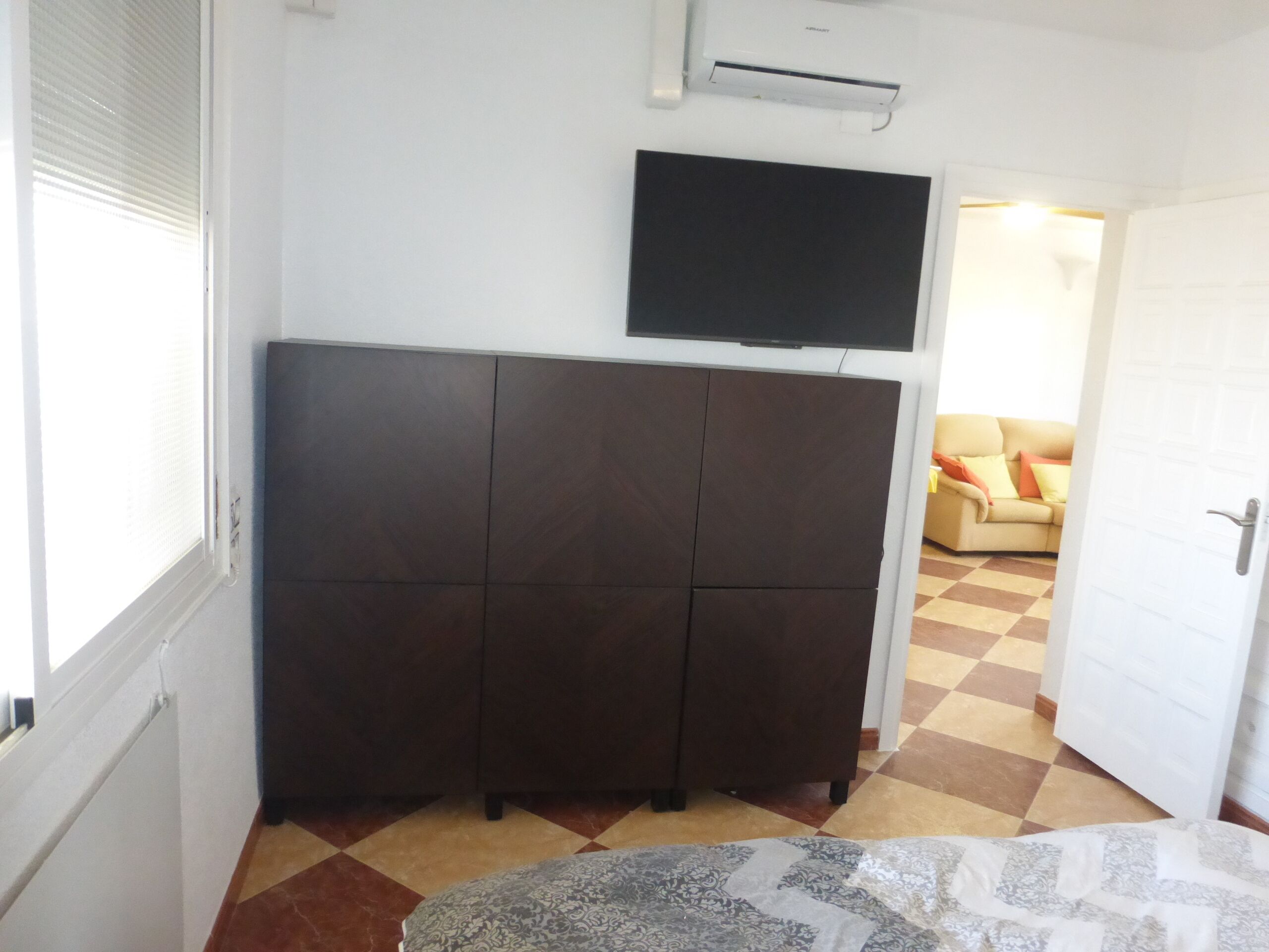 Una habitación con un armario de madera oscura, un televisor de pantalla plana en la pared y un piso a cuadros.