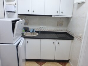 A compact kitchen with white cabinets, a black countertop, a sink, and a white refrigerator. - 1 Bedroom Apartment at 50 Meters From the Beach (Roquetas de Mar)