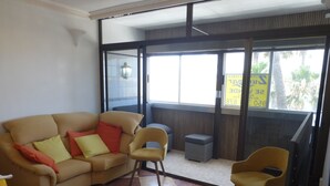 A room with a beige sofa, two armchairs, a small table, and a window with a view of palm trees. - 1 Bedroom Apartment at 50 Meters From the Beach (Roquetas de Mar)