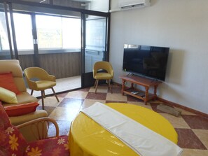 Ein Zimmer mit Fernseher, zwei gelbe Stühle, einem Sofa mit orangefarbenen Kissen und einem karierten Boden.
