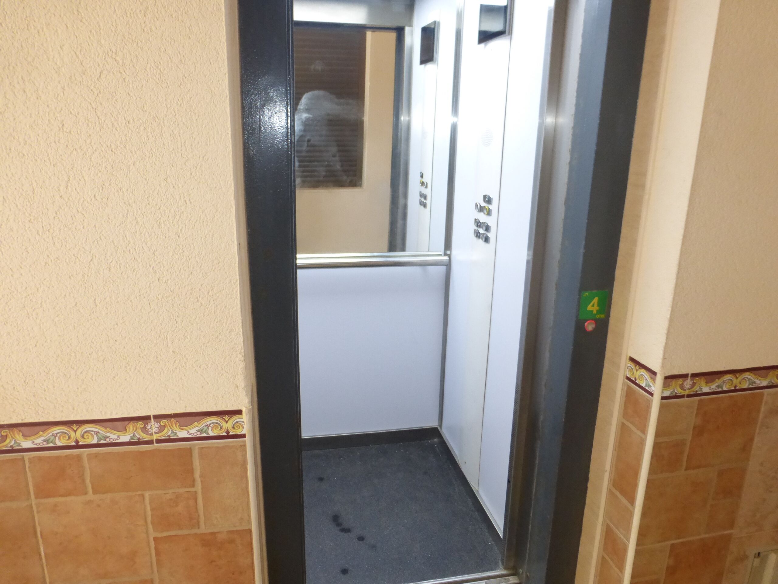 Interior de elevador com chão de azulejos, corrimão e porta com a inscrição '4'.