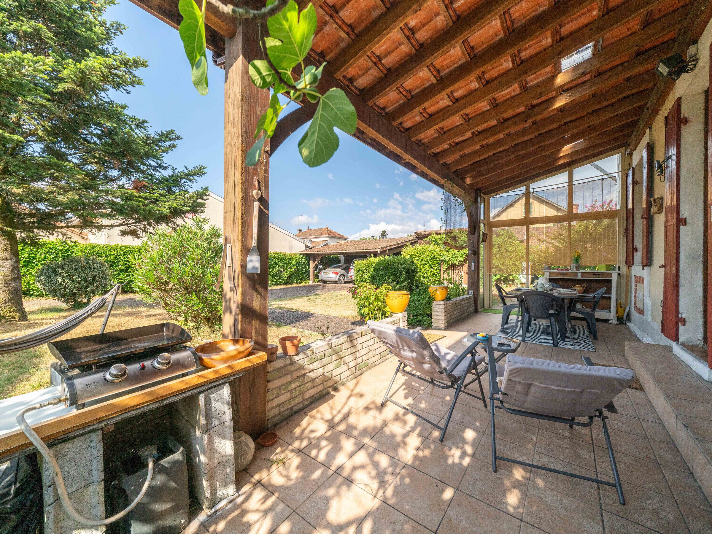 Un patio exterior con una parrilla, asientos y vistas al jardín trasero.