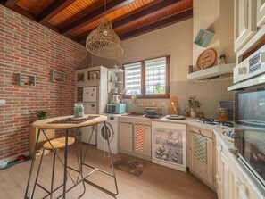 A kitchen with a brick wall, wooden beams, a hanging light fixture, a washing machine, a microwave, and a stove. - Charming house with AC, pets OK - 4 guests (Parentis-en-Born)