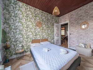 A bedroom with a large bed, a wooden headboard, a brick wall, and a door leading to a dining area. - Charming house with AC, pets OK - 4 guests (Parentis-en-Born)