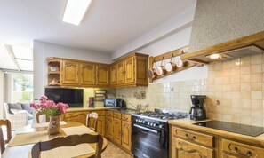A kitchen with wooden cabinets, a stove, and a dining area with a table and chairs. - Spacious house with parking - 6 guests (Les Loges-Marchis)