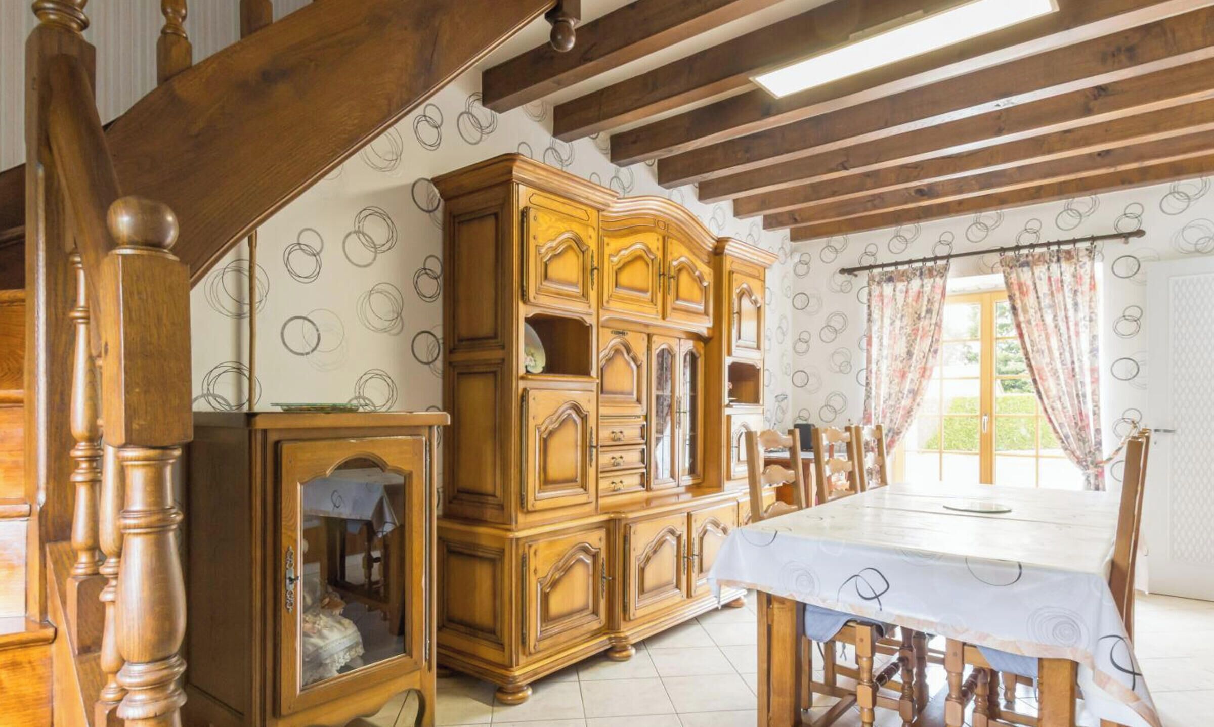 Une salle à manger avec une table et des chaises en bois, un grand meuble en bois et un escalier avec des balustrades en bois.