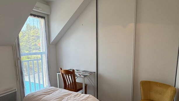 Un dormitorio con cama, escritorio, silla y ventana con vistas a árboles.
