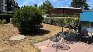 Un patio con mobiliario exterior, una sombrilla grande y un seto.