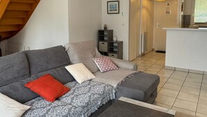 Una sala moderna con un sofá gris, un plaid estampado y una almohada roja. Una escalera se ve a la izquierda, que sube a un nivel superior.