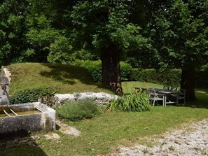 Ein ruhiger Außenbereich mit einer Steinstruktur, einem Tisch mit Stühlen und einer sanften Grasfläche.