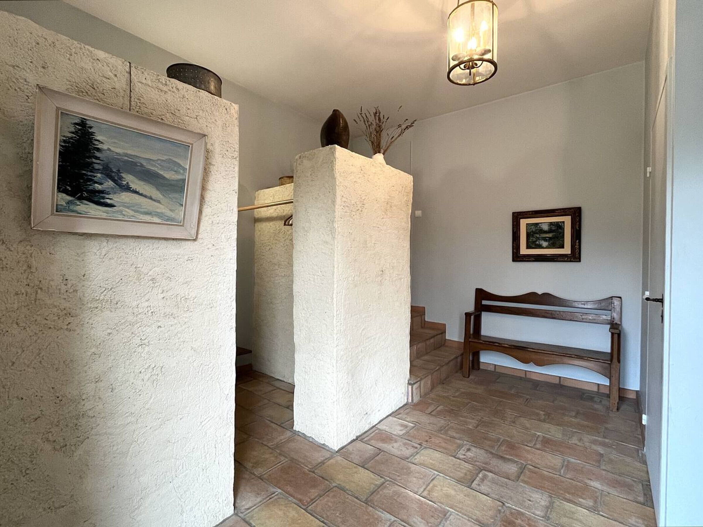 A hallway with a stone pillar, a wooden bench, and a staircase leading to another room.