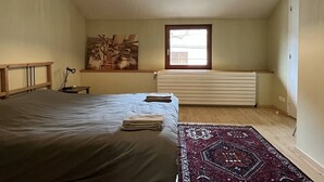 Ein Schlafzimmer mit Bett, Heizkörper, Fenster und einer Pendelleuchte.