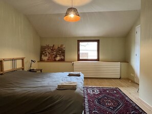 Ein Schlafzimmer mit Bett, Heizkörper, Fenster und einer Pendelleuchte.