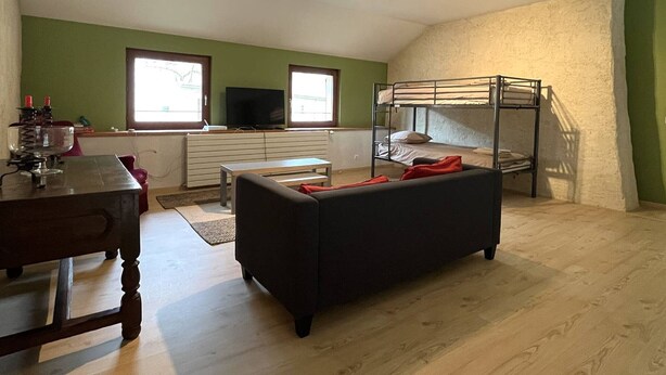 Ein Zimmer mit einem Etagenbett, einem Fernseher, einem Esstisch und einem Sofa.