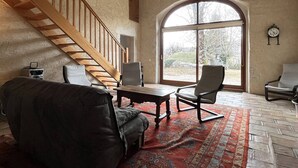Ein geräumiger Raum mit einer Holztreppe, einem großen Bogenfenster und einer traditionellen Uhr an der Wand.