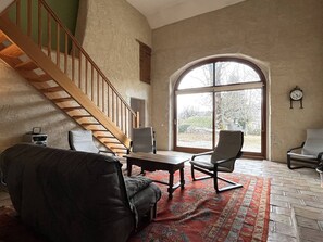 Ein geräumiger Raum mit einer Holztreppe, einem großen Bogenfenster und einer traditionellen Uhr an der Wand.