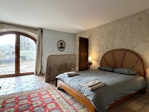 A bedroom with a bed, a nightstand, a lamp, a rug, and a view through a door.