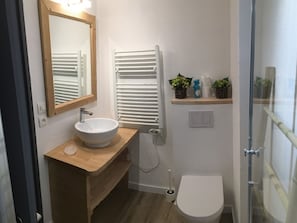 Ein modernes Badezimmer mit einem Holzkosmetikschrank, einem weißen Waschbecken, einem Spiegel, einem Handtuchhalter, einer Toilette und einem Duschbereich.