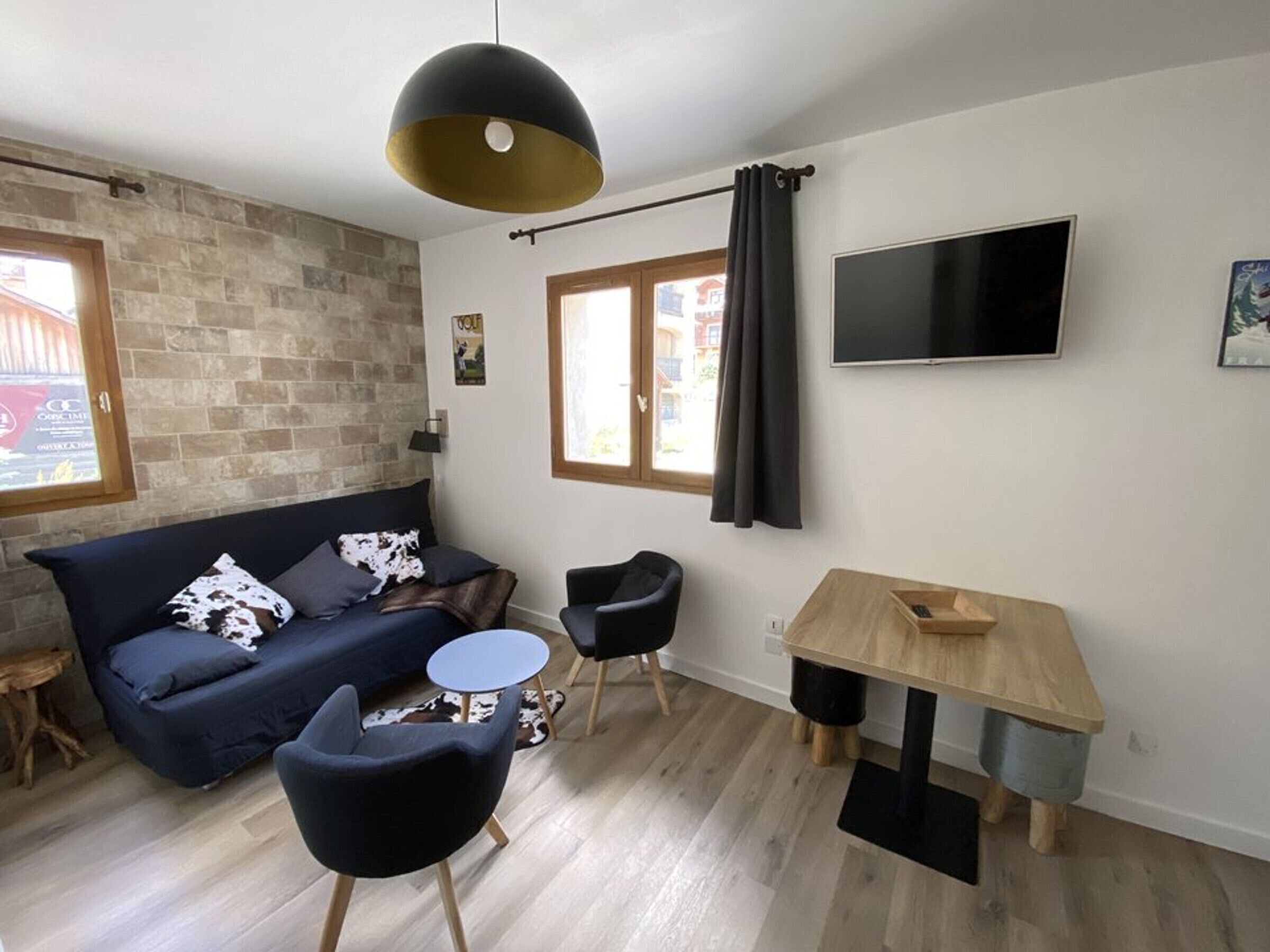 A modern living room with a sofa, two chairs, a small round table, a TV, and a window with curtains.