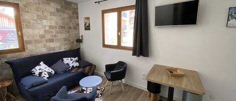 A modern living room with a sofa, two chairs, a small round table, a TV, and a window with curtains.