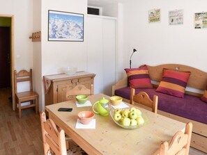 Ein gemütliches Zimmer mit einem Holzesstisch, Stühlen, einer Couch mit bunten Kissen und einem Wandbild.