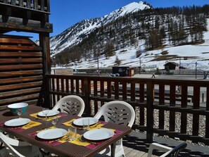 Eine Holzterrasse mit Esstisch, mit Blick auf eine verschneite Berglandschaft.
