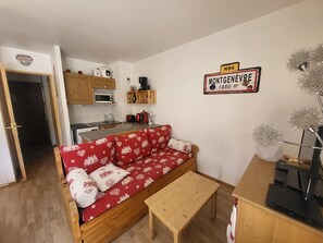 A cozy living room with a red sofa, wooden coffee table, and a kitchen in the background. - Apartment "La Doire" on the slopes - 3 guests (Montgenèvre)