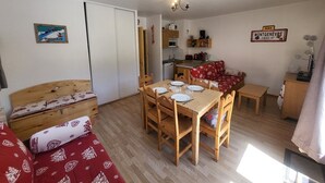 Un espacio habitable compacto con una mesa de comedor, muebles de madera, una kitchenette y un sofá rojo.