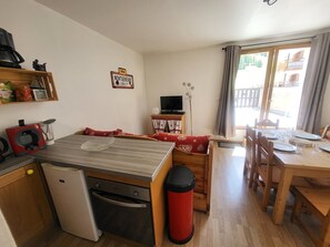 A compact kitchen with a refrigerator, stove, and a coffee machine. There is a dining area with a table set for four, and a TV on a small stand. - Apartment "La Doire" on the slopes - 3 guests (Montgenèvre)