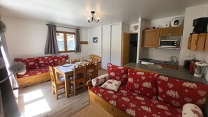 Una sala de estar acogedora con un sofá rojo estampado, una mesa de comedor de madera y una cocina con armarios de madera y un microondas.
