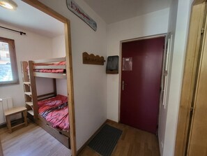 A dormitory room with a bunk bed, a desk, a red door, and a small window. - Apartment "La Doire" on the slopes - 3 guests (Montgenèvre)
