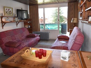 Una sala de estar con un sofá, una mesa de centro, un televisor y vistas al exterior.
