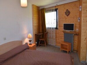 A room with a bed, a desk with a computer, a chair, a lamp, and a television. - Apartment with village and slopes view - 6 guests (Montgenèvre)