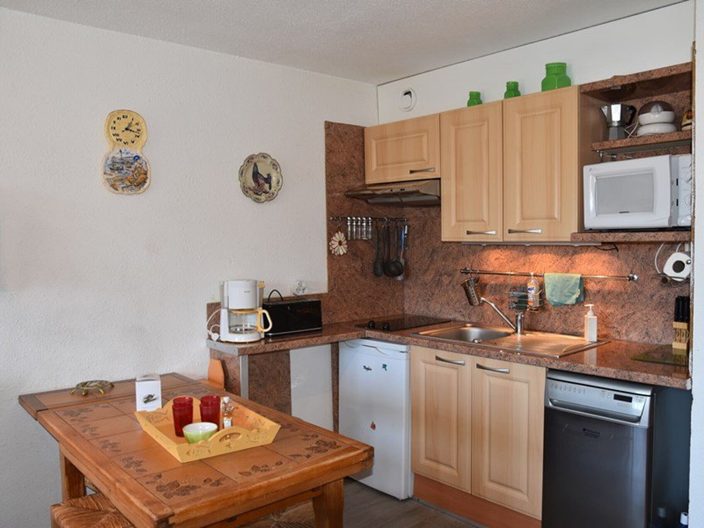 Cocina compacta con armarios de madera, microondas, cafetera y lavavajillas.
