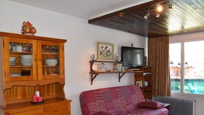 A living room with a wooden cabinet, a television, a sofa, and a window with a view of buildings. - Apartment with village and slopes view - 6 guests (Montgenèvre)