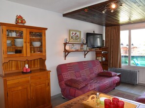 Ein Wohnzimmer mit einem Holzkabinett, einem Fernseher, einem Sofa und einem Fenster mit Blick auf Gebäude.