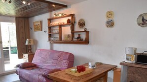 A cozy living area with a sofa, wooden table, and chairs. A coffee maker and trash can are on the counter. - Apartment with village and slopes view - 6 guests (Montgenèvre)