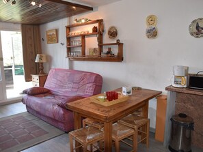 Ein gemütlicher Wohnbereich mit einer Couch, einem Holztisch und Stühlen. Auf der Arbeitsfläche befinden sich eine Kaffeemaschine und ein Mülleimer.
